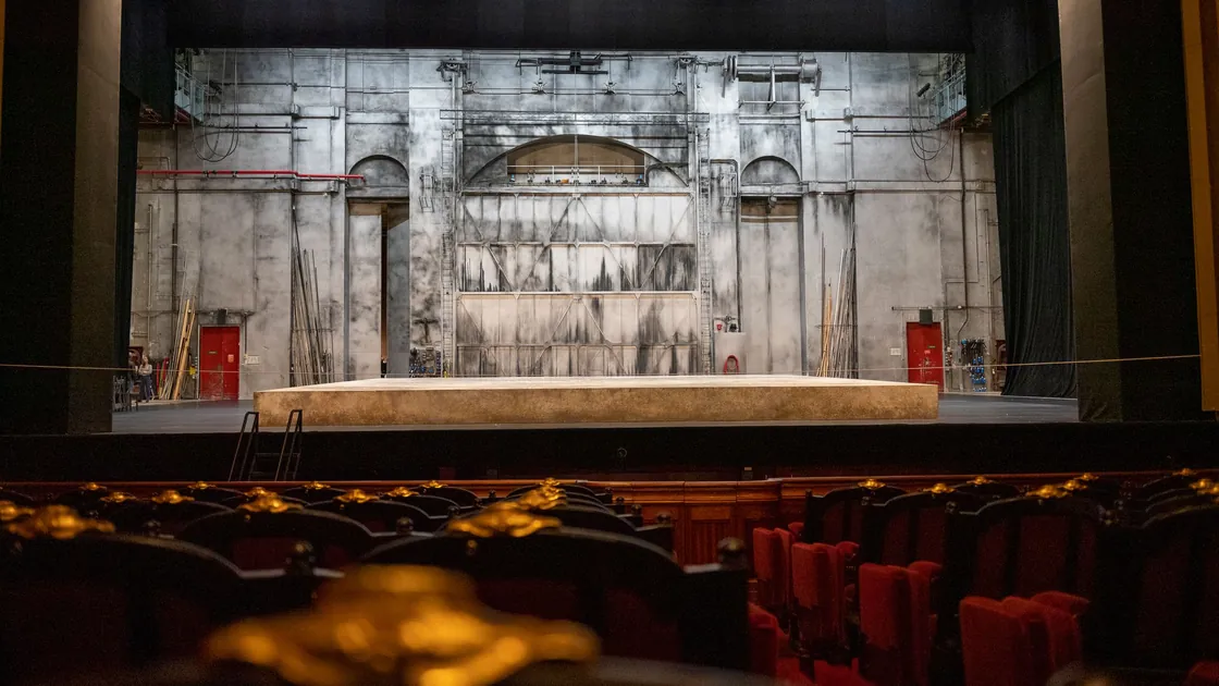 Escenario vacío visto desde la platea, con un practicable de madera y un fondo pintado con textura de muro gastado.